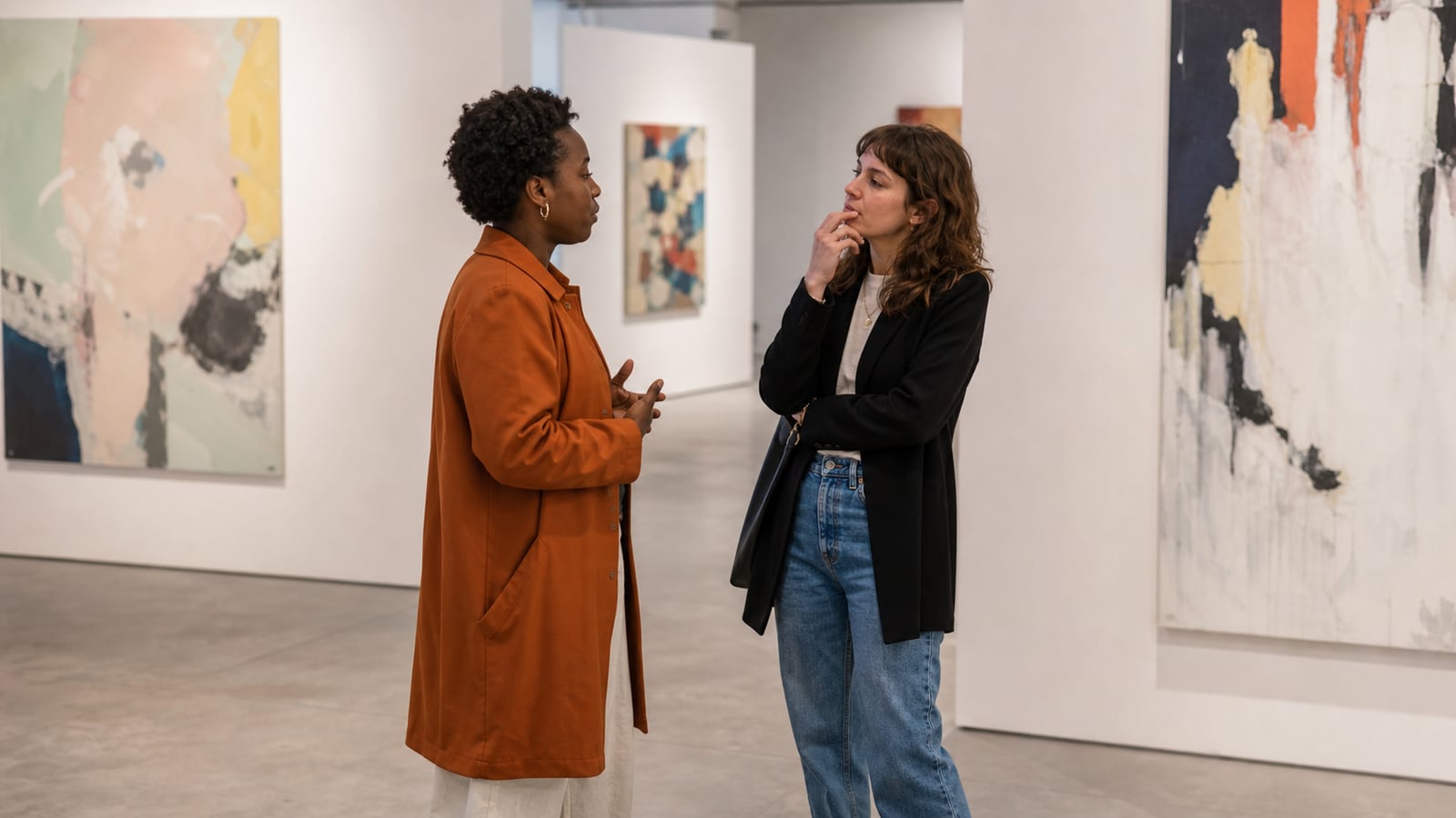 Twee bezoekers bespreken een tentoonstelling naast abstracte schilderijen